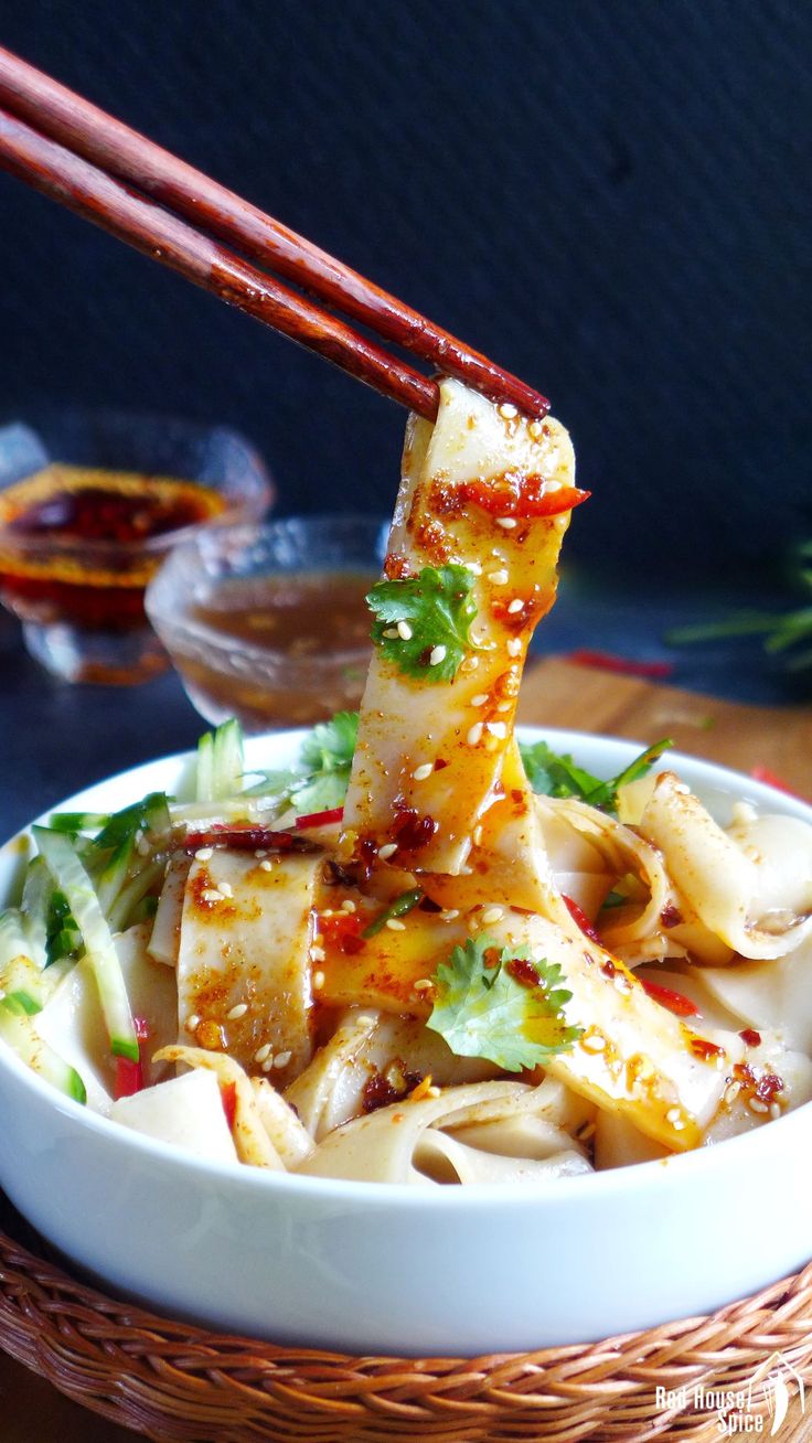 a bowl filled with noodles and chopsticks on top of a wooden table next to sauce