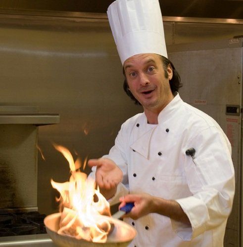 a man in a chef's hat is cooking something on a pan with flames