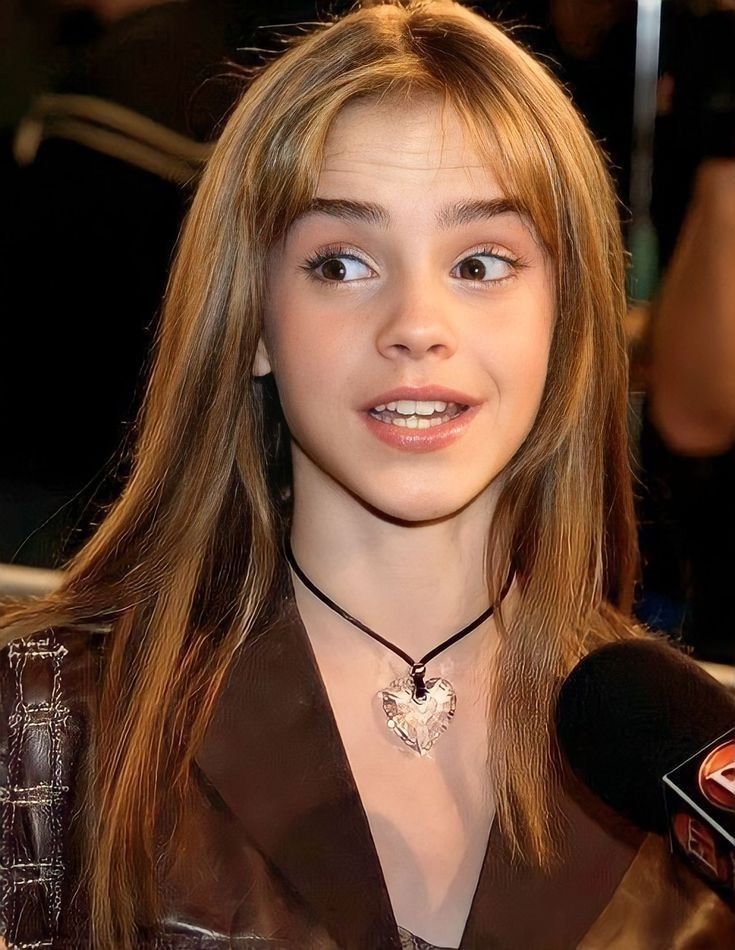 a young woman with long hair wearing a brown shirt and black necklace holding a microphone in front of her