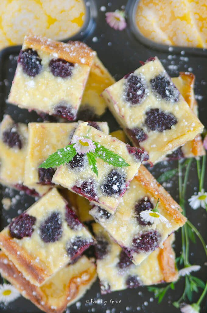 blueberry cheesecake squares with mint sprinkles on a black tray surrounded by flowers