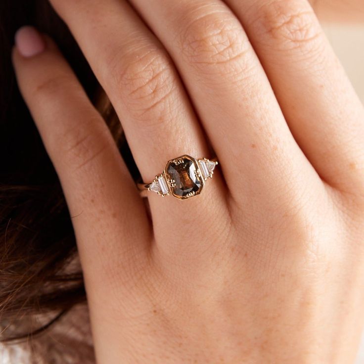 a close up of a person's hand wearing a gold ring with an oval shaped brown and white diamond