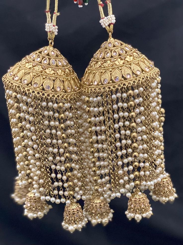 two golden bells with pearls hanging from it's sides on a black background,