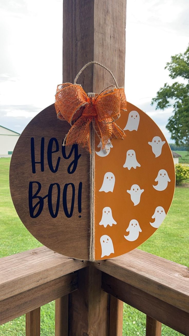 a wooden sign that says hey boo with ghost faces on it and an orange bow