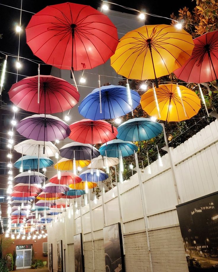 many colorful umbrellas hanging from the ceiling in an open area with lights on them