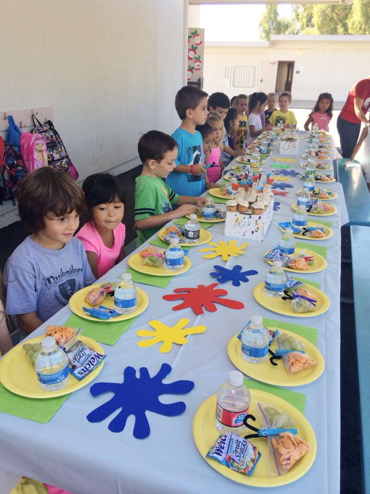 a group of children sitting at a table with plates and cups on it, all ready to eat