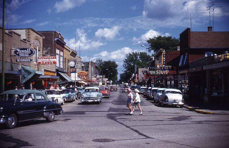 people crossing the street in front of cars on a city street with shops and businesses