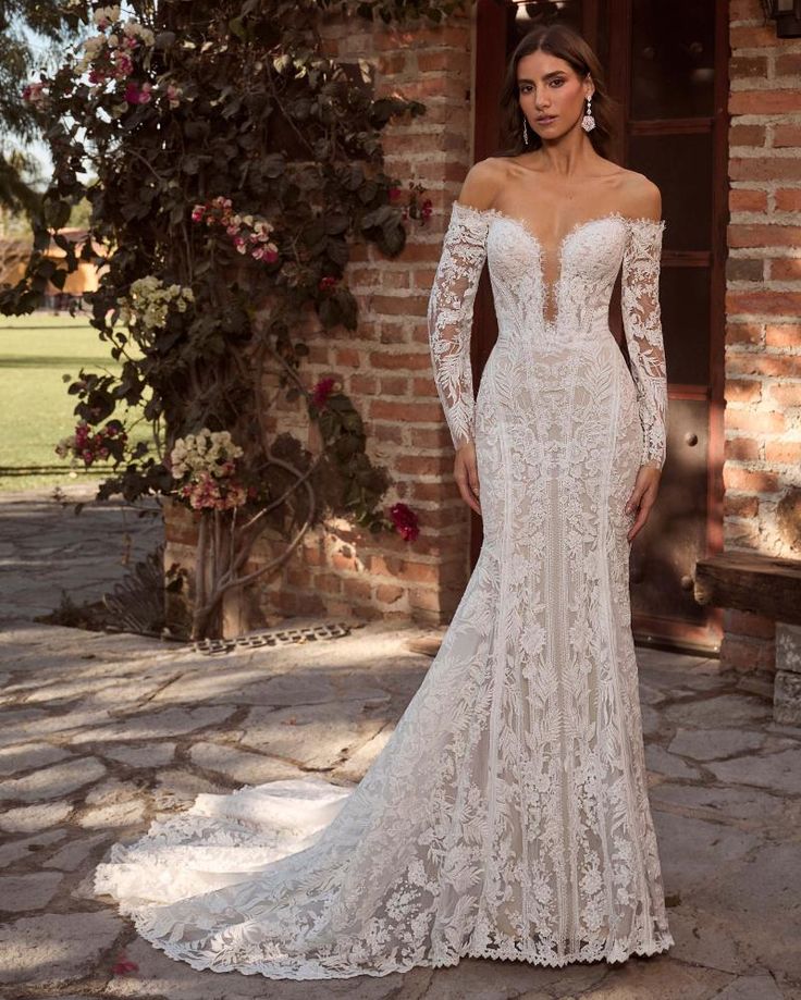 a woman standing in front of a brick building wearing an off the shoulder wedding dress