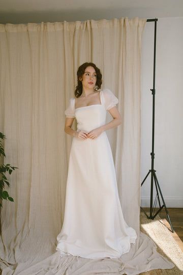 a woman is standing in front of a curtain wearing a white dress and holding her hands on her hips