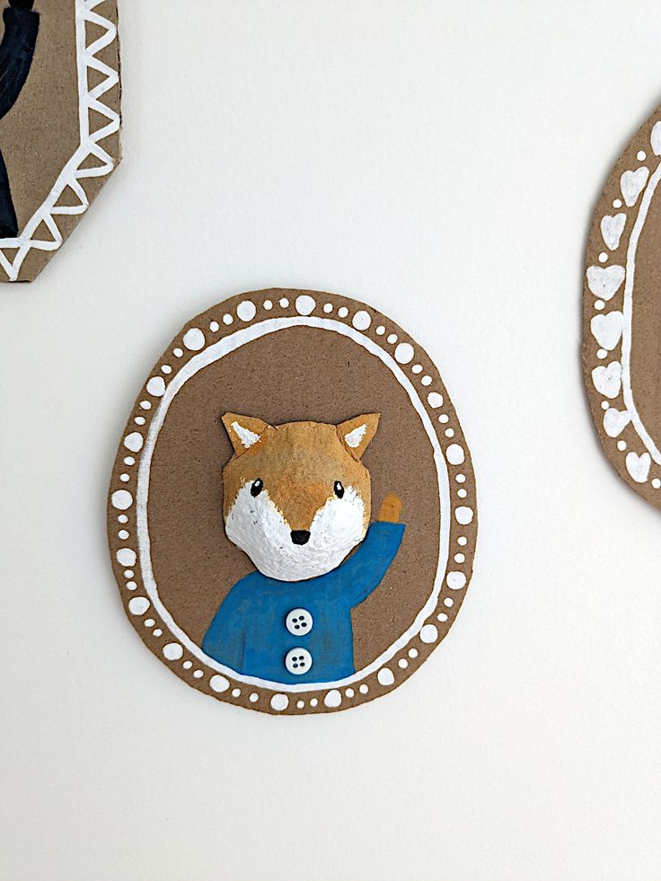 some paper cutouts are hanging on the wall next to each other, including one with a fox head and another with a blue coat