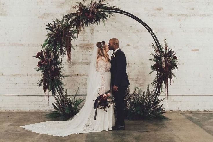 a bride and groom standing in front of an arch decorated with greenery