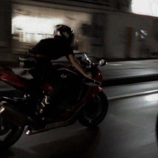 a man riding on the back of a red motorcycle down a city street at night