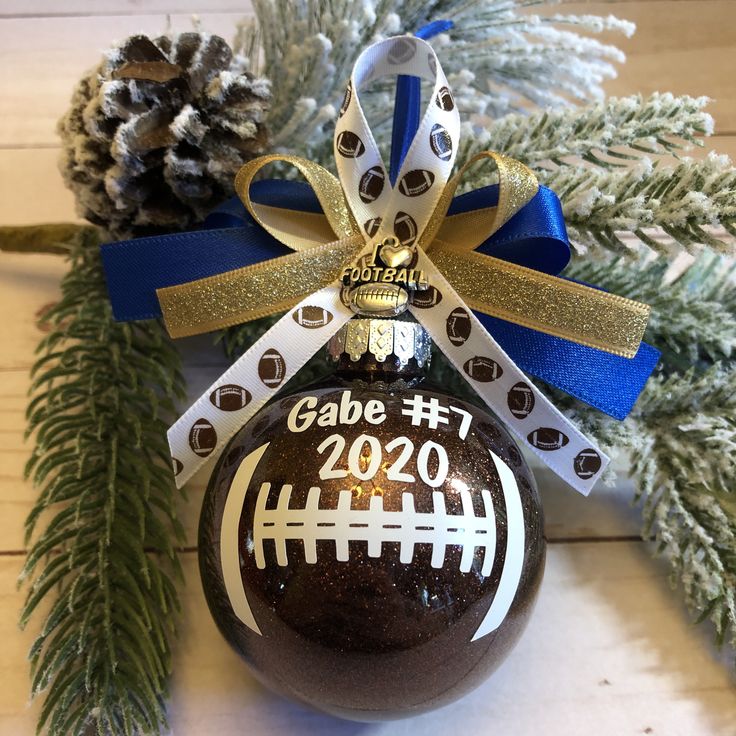 a football ornament hanging from a christmas tree with blue ribbon and pine cones