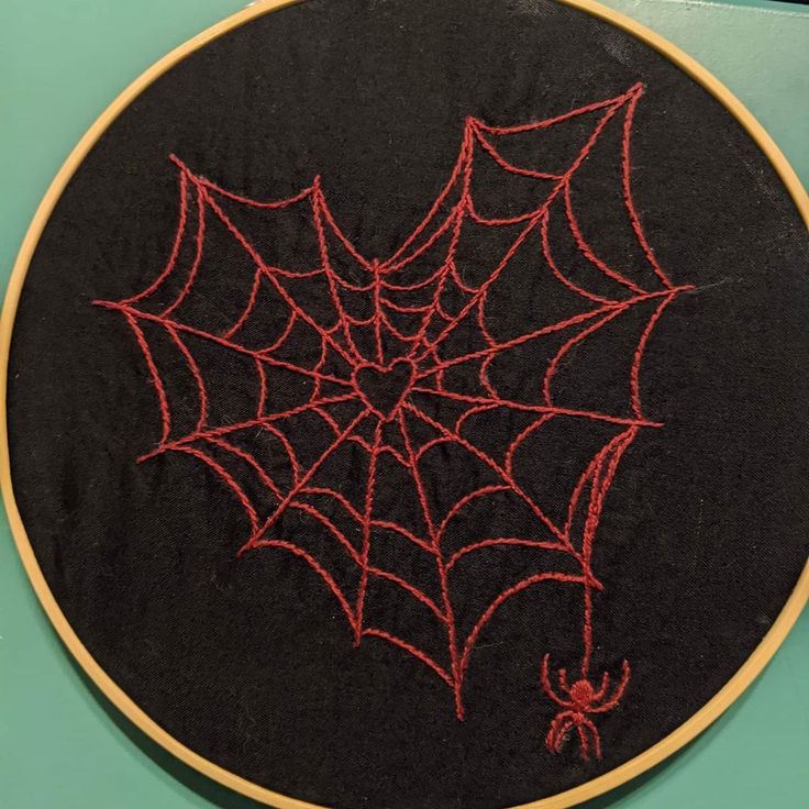 an embroidered spider web on a black cloth with red thread in the center, sitting on top of a wooden hoop