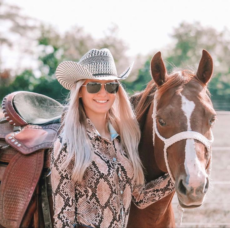 a woman in cowboy hat and sunglasses standing next to a horse