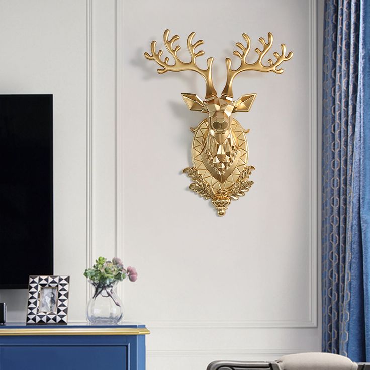 a gold deer head mounted to the side of a white wall next to a blue dresser