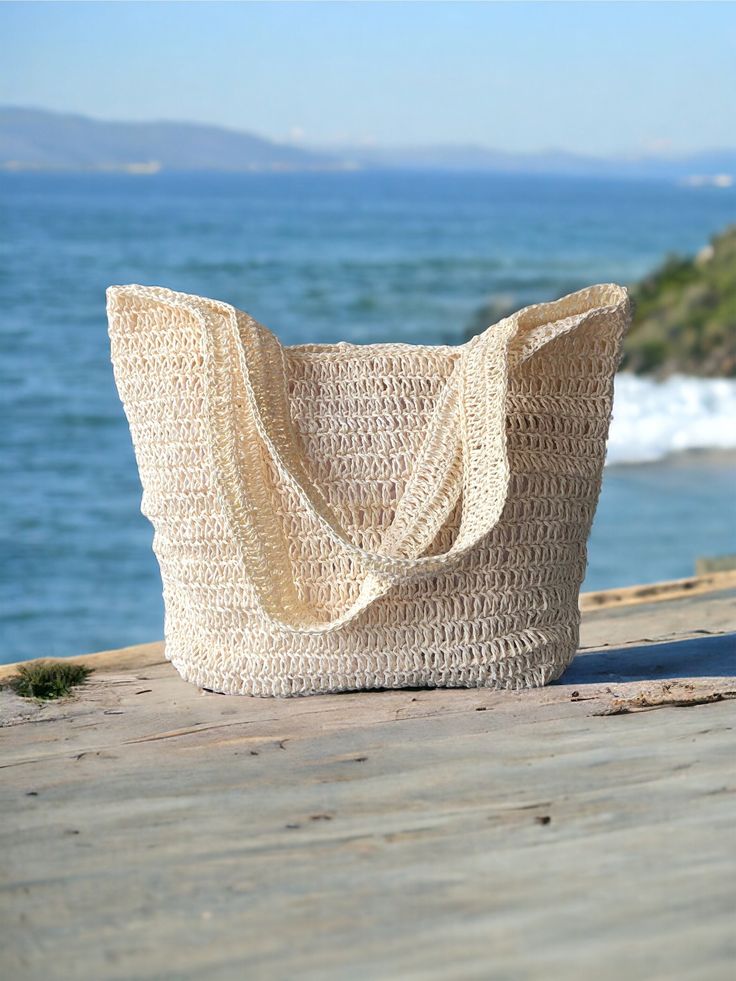 a straw bag sitting on top of a wooden table next to the ocean and mountains