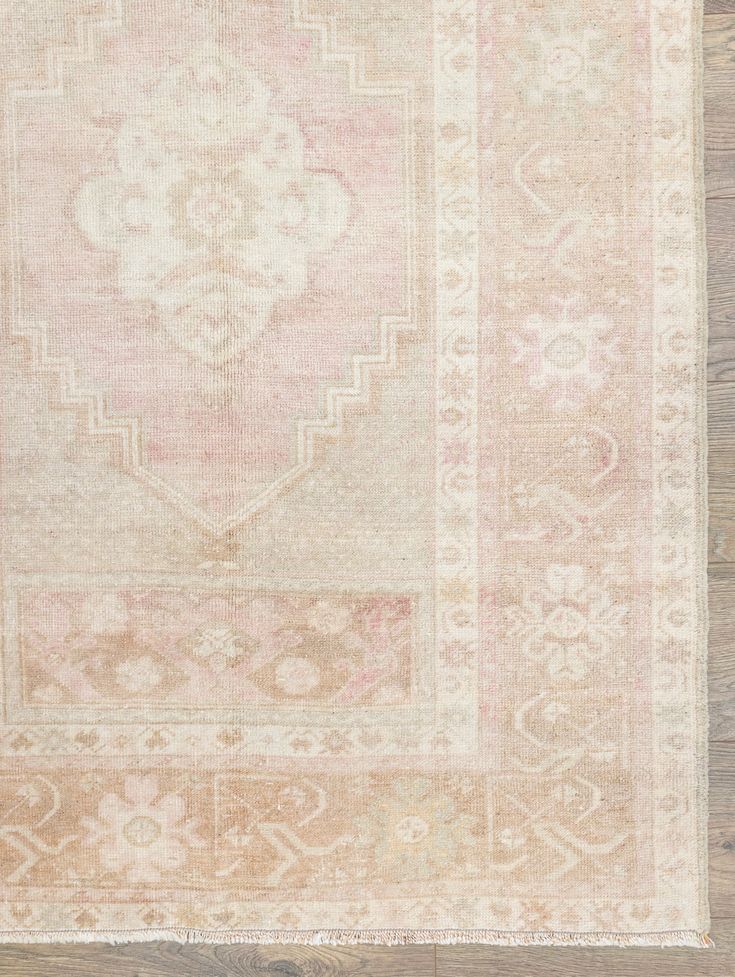 an antique rug with pink and beige colors on a wooden floor in front of a wall