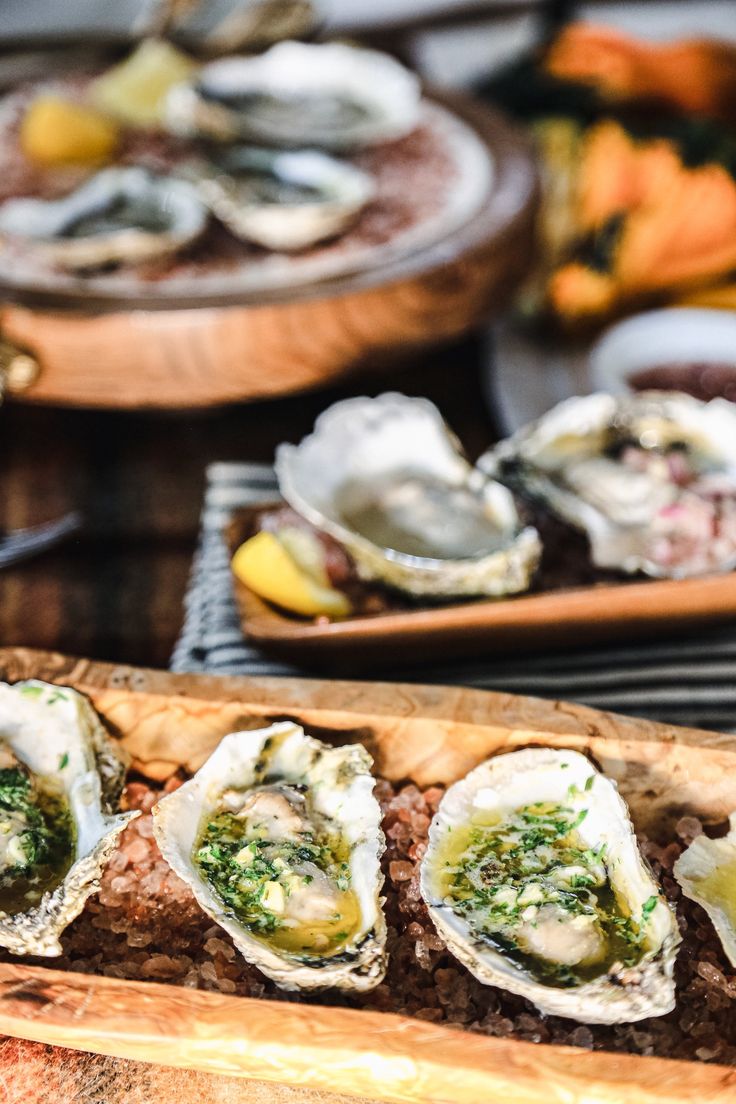 an assortment of oysters on a wooden platter with other dishes in the background