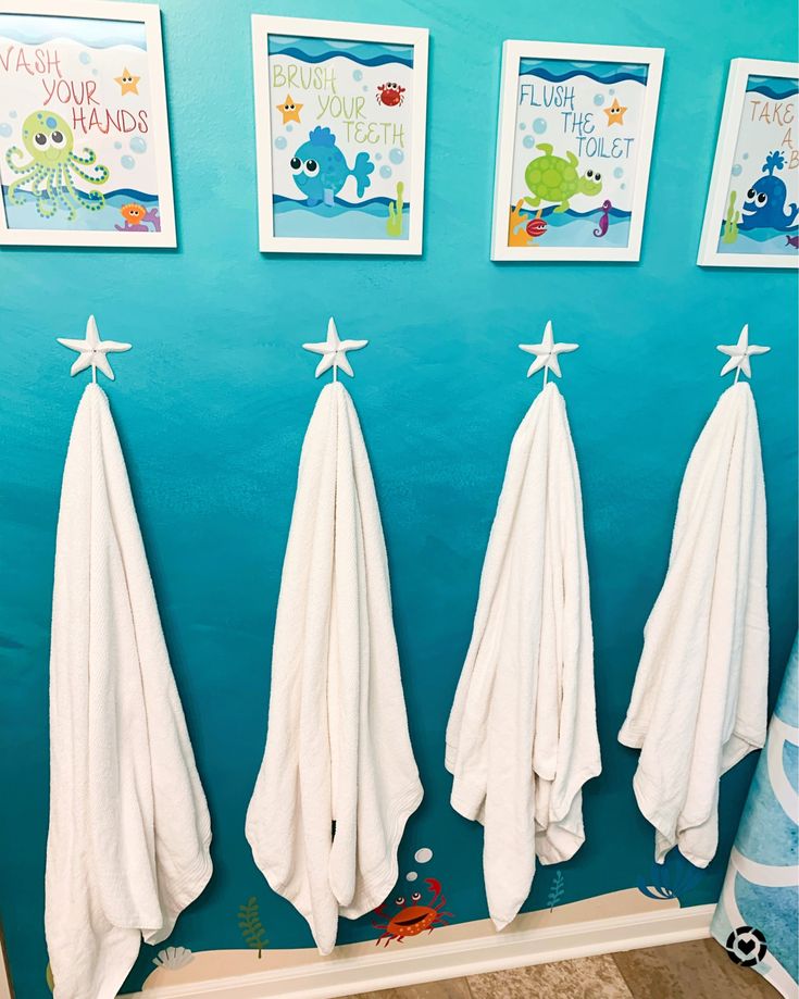 three white towels hanging on the wall in a children's bathroom with pictures above them