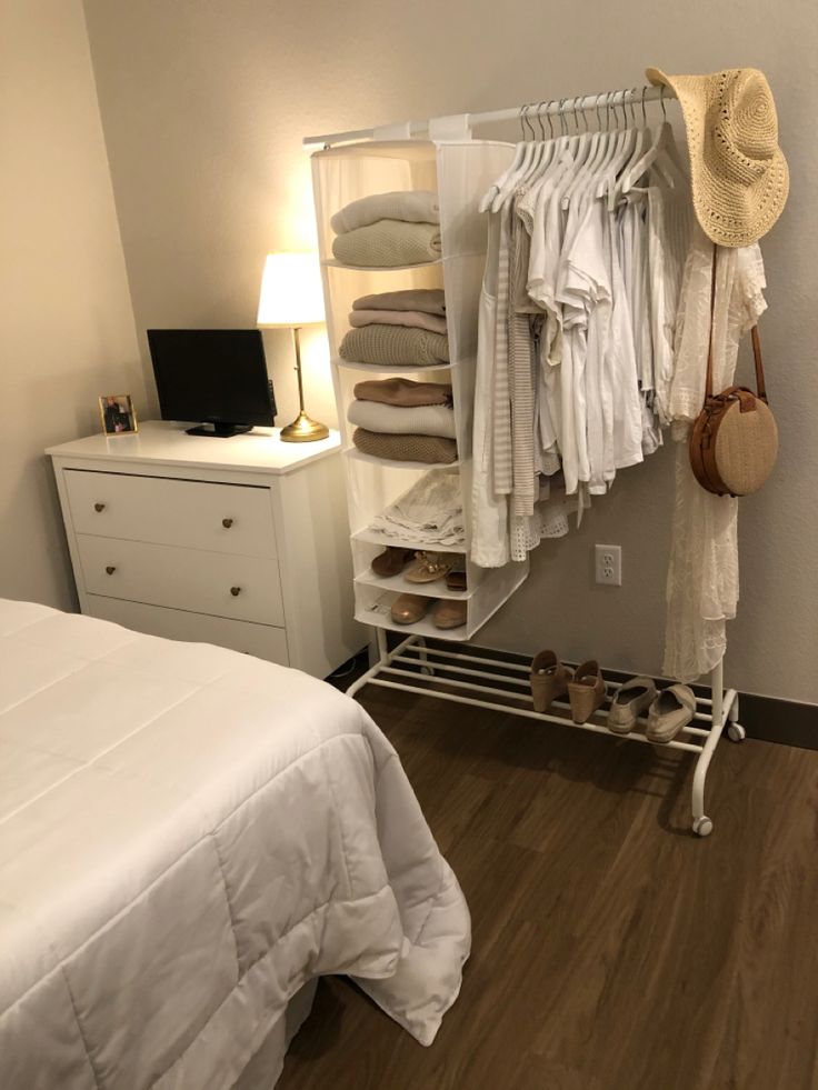 a white bed sitting next to a closet with clothes hanging on it's rails