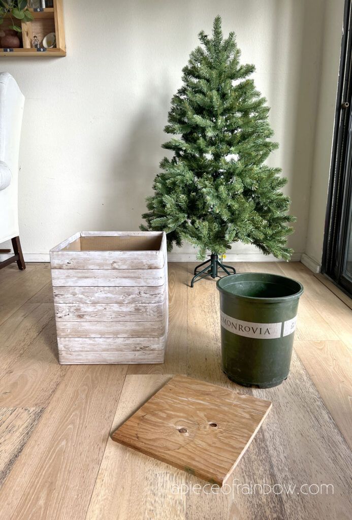 a small christmas tree sitting on top of a wooden floor next to a bucket and box