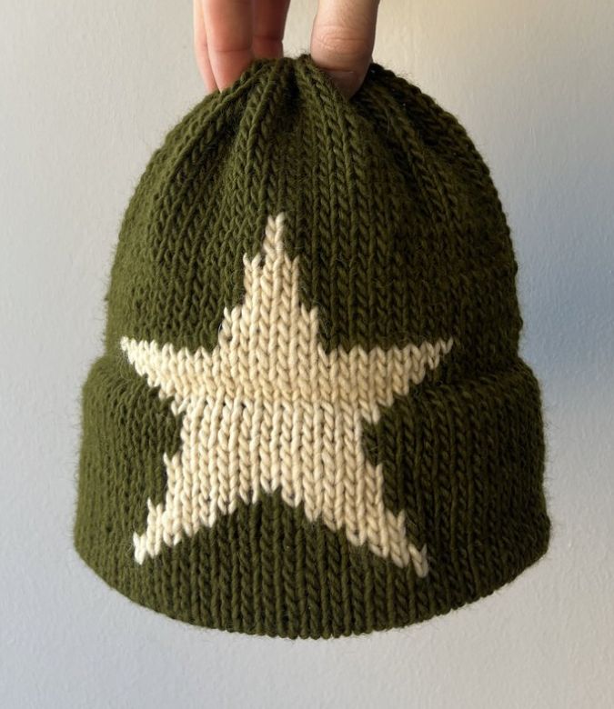 a hand holding up a green knitted hat with white stars