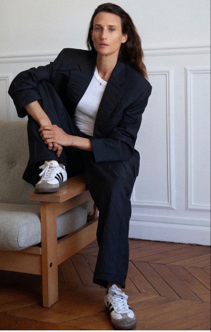 a woman sitting on top of a wooden chair with her legs crossed and wearing white sneakers