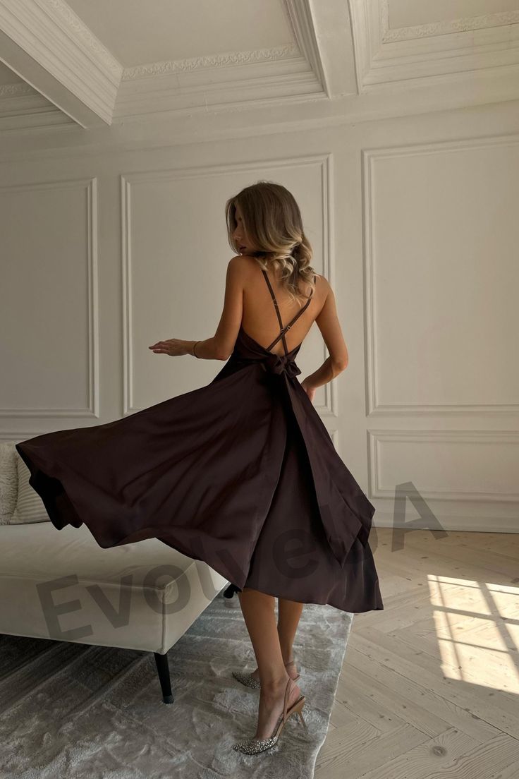 a woman in a brown dress is standing near a couch and looking at the wall