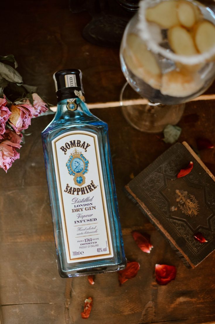 a bottle of alcohol sitting on top of a table next to flowers and an open book