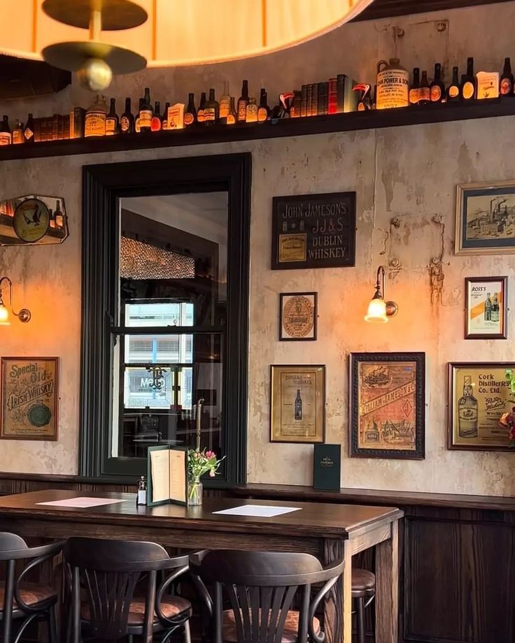 an empty restaurant with wooden tables and chairs in front of the wall full of bottles