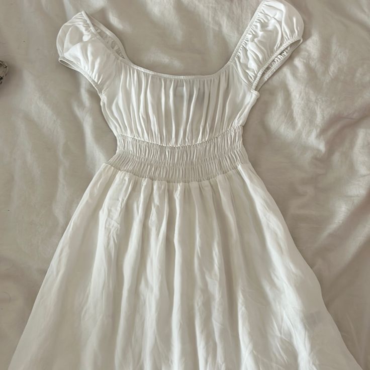 a white dress laying on top of a bed next to a pair of shoes and a purse