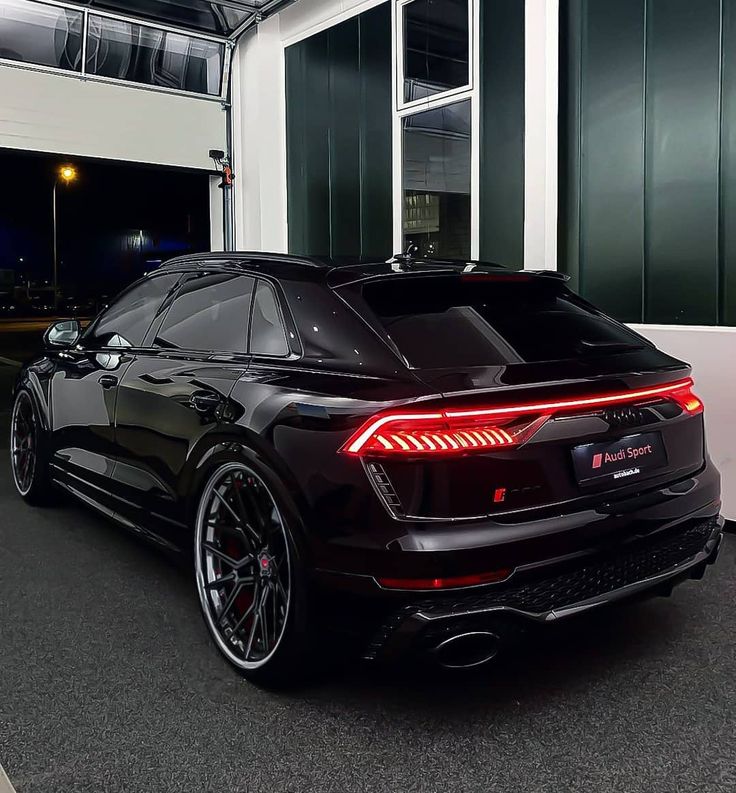 the rear end of a black car parked in front of a large building at night