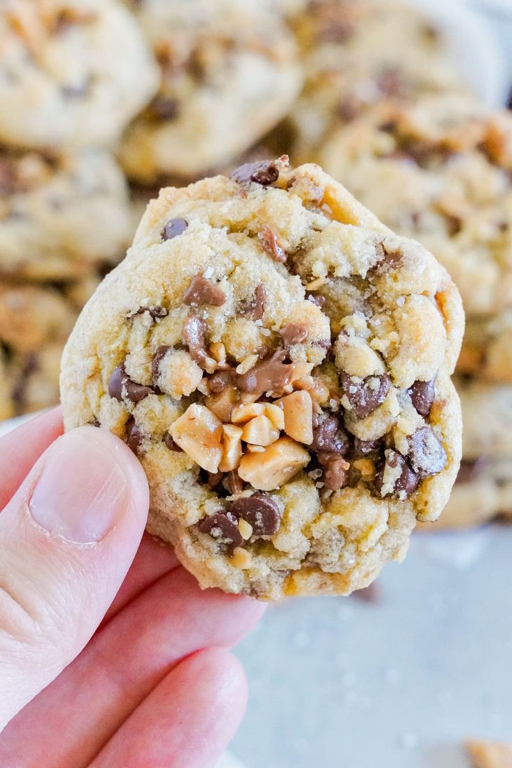 a hand holding up a cookie with nuts and chocolate chips on it in front of other cookies