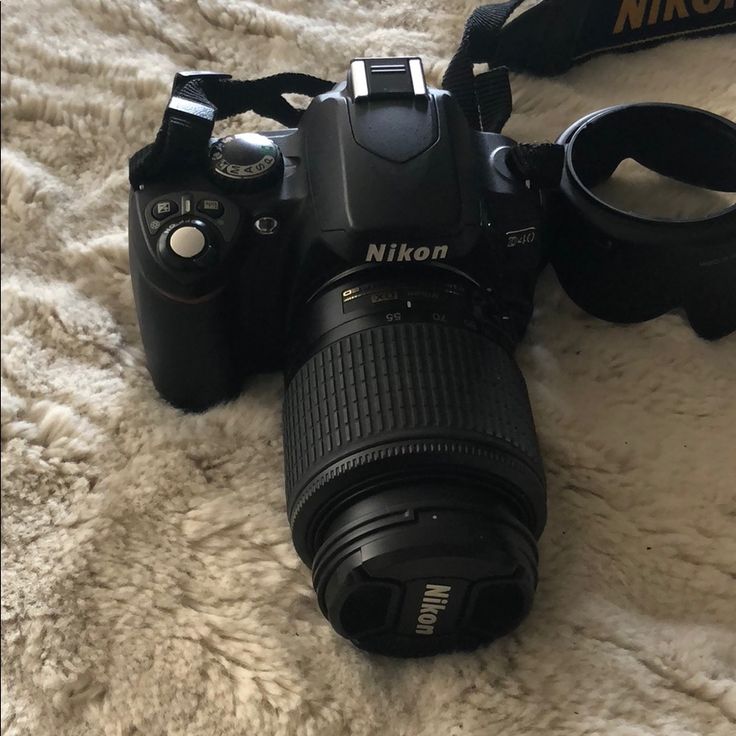 a camera sitting on top of a bed next to a bag and lens cap with the nikon logo on it