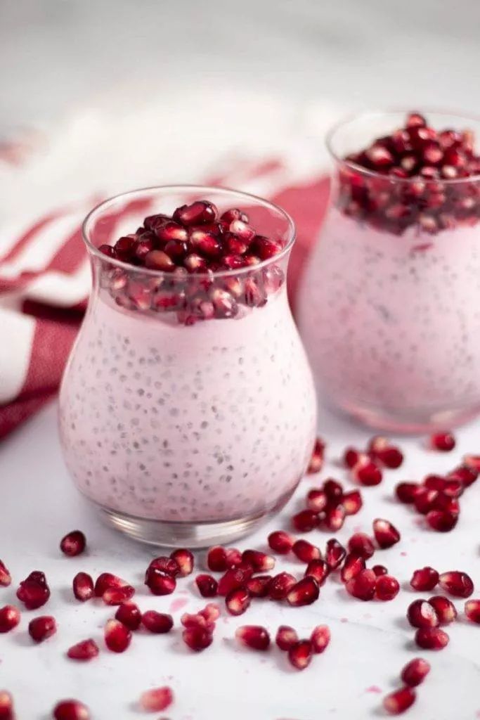 two small glasses filled with pudding and pomegranates on top of a table