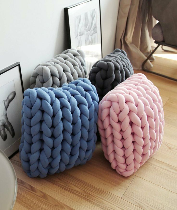 four different colored knitted pillows sitting on the floor