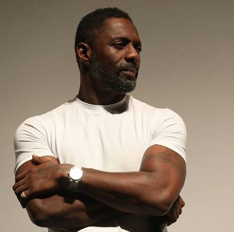 a man with his arms crossed standing in front of a white wall wearing a watch