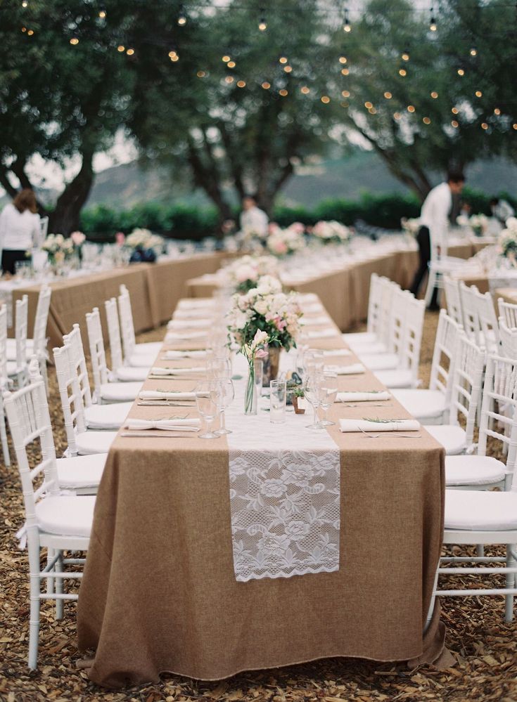 a long table with white chairs and tables covered in brown linens is set up for an outdoor wedding reception