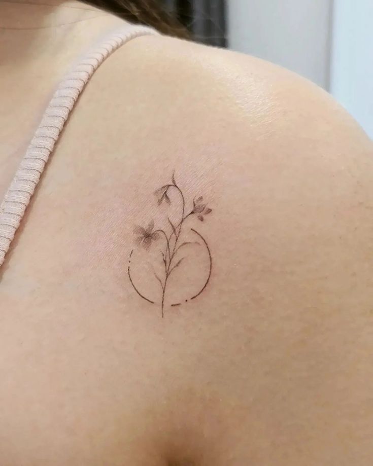 a woman's shoulder with a small flower tattoo on the left side of her breast