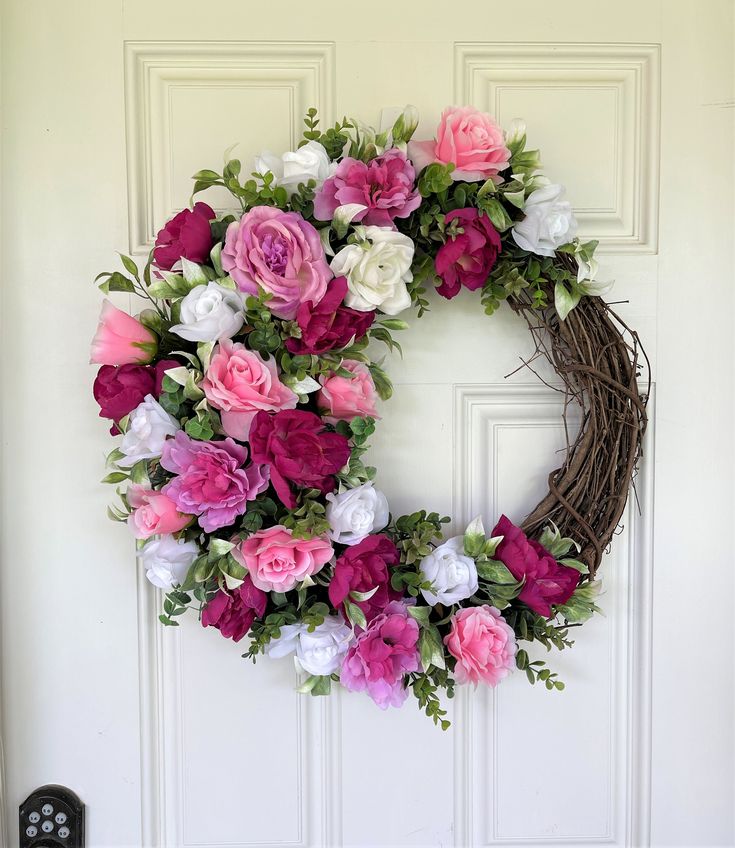 a wreath with pink and white flowers hanging on a door