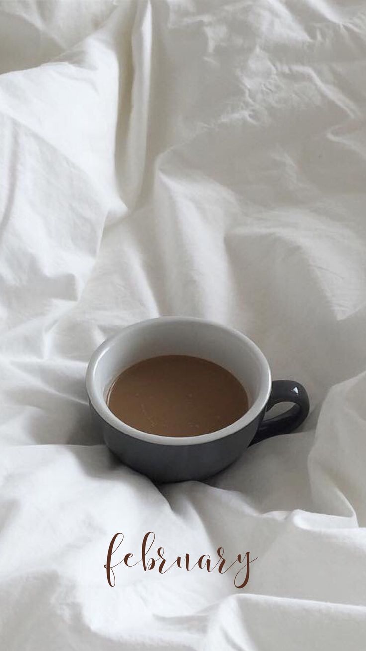 a cup of coffee sitting on top of a white sheet covered tablecloth with the words february written below it