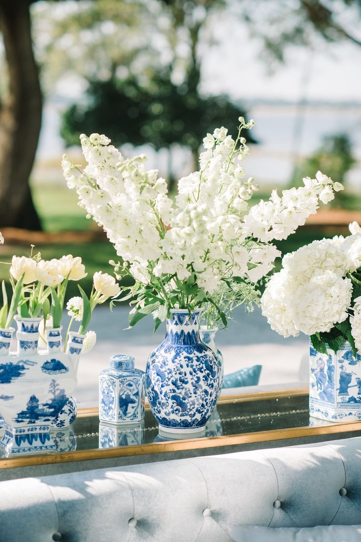 white flowers in blue and white vases sitting on a table with an upholstered bench