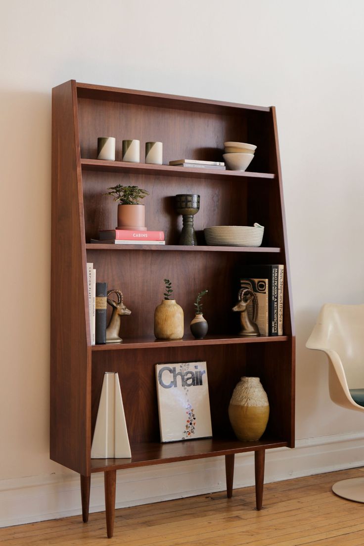 a wooden shelf with books and vases on it in a room next to a chair