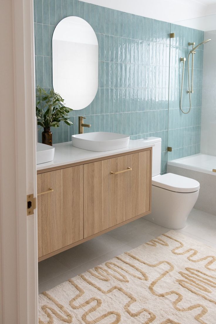 a white toilet sitting next to a bath tub under a bathroom mirror on top of a wooden cabinet