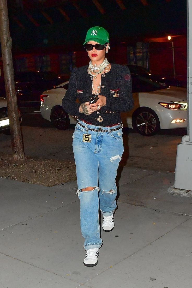 a woman in ripped jeans and a green hat is walking down the street at night