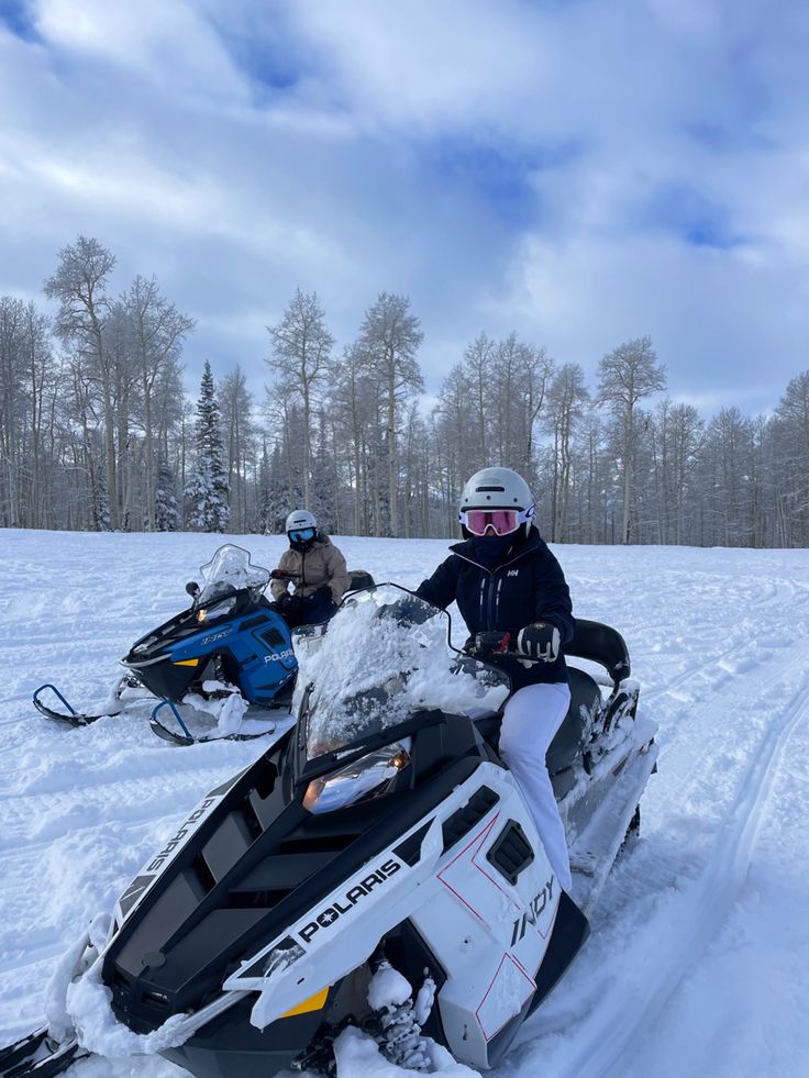 two people riding snowmobiles in the snow