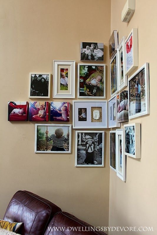 a living room wall filled with pictures and framed photos on the wall next to a brown leather couch