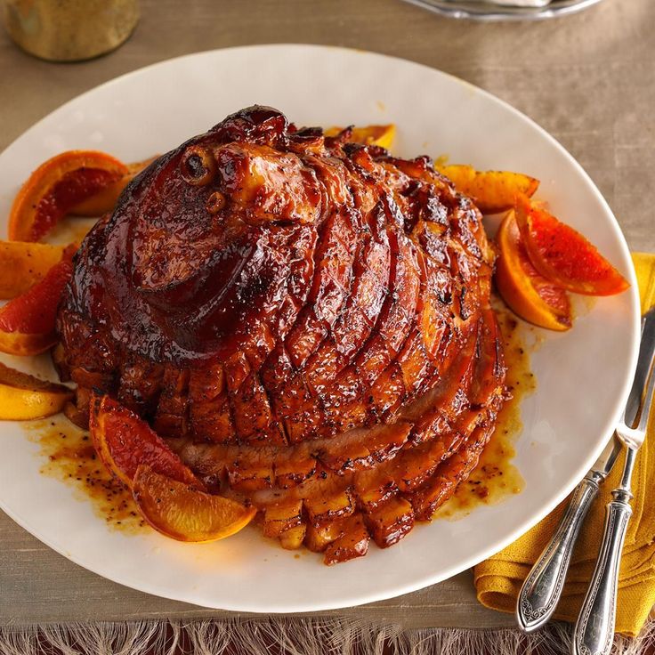 a white plate topped with meat covered in sauce and sliced oranges next to silverware