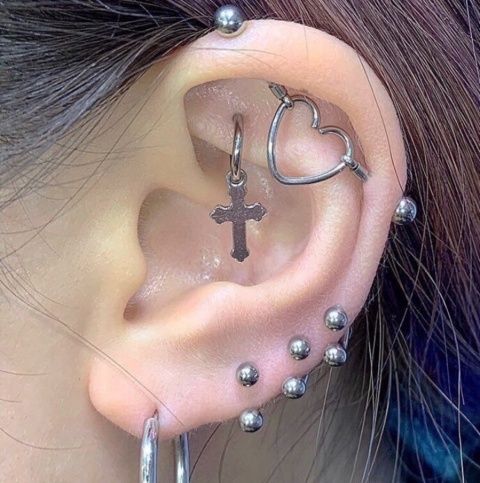 a woman with piercings on her ear wearing a cross and heart shaped hoop earrings