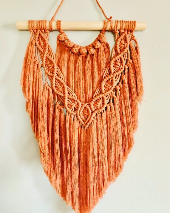 an orange piece of art hanging from a wooden hanger on a white wall with some string attached to it